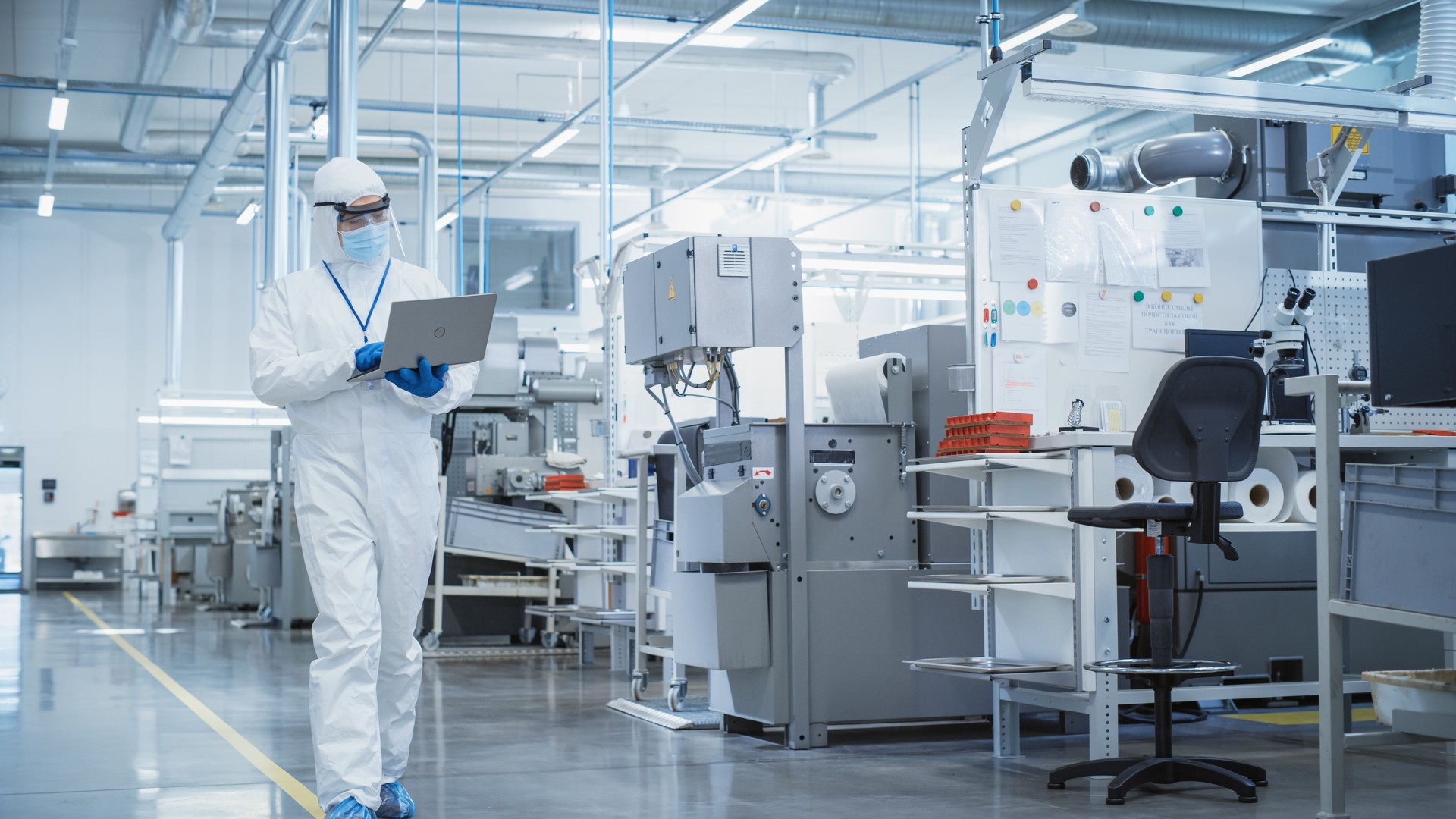 Heavy Industry Manufacturing Factory: Scientist in Sterile Coverall Walking with Laptop Computer, Examining Industrial CNC Machine Settings and Configuring Production Functionality.