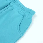 Close-up of custom baby joggers side detail, showing premium elastic waistband construction, reinforced curved pockets, and high-density cotton fleece fabric. Professional infant sweatpants manufacturing by an expert clothing factory.