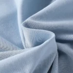 Close-up of premium baby blue romper fabric, featuring ultra-soft breathable cotton jersey, high-density smooth texture, and eco-friendly dyeing. Professional infant apparel textile from an expert clothing manufacturer.