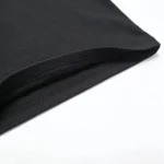Precision double-needle bottom hem on a black heavyweight cotton T-shirt, clean edge finishing from a professional OEM/ODM clothing manufacturer, durable industrial-grade apparel construction.