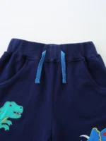 Close-up of navy baby shorts detail, featuring contrast light blue drawstrings, a secure elastic waistband, and vibrant dinosaur screen printing. High-quality infant boy's apparel construction from a professional clothing manufacturer.