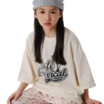 Custom girls' oversized T-shirt in off-white, vintage graphic print with palm tree and "LA Tropical" lettering, trendy boxy fit, premium heavyweight cotton, professional OEM/ODM kids streetwear factory.