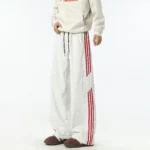 White wide-leg track pants with red side stripes and drawstring waist, produced by a professional OEM/ODM streetwear manufacturer.