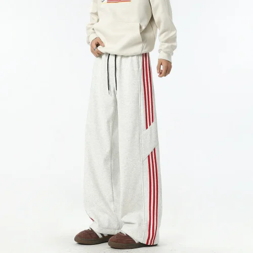 White wide-leg track pants with red side stripes and drawstring waist, produced by a professional OEM/ODM streetwear manufacturer.